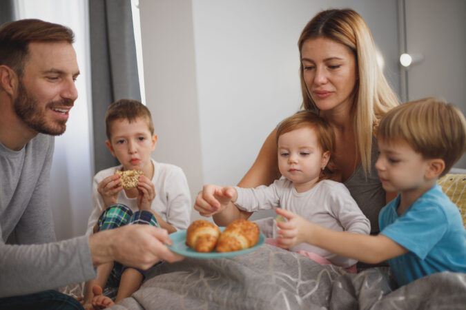 Family eating croissants on bed.