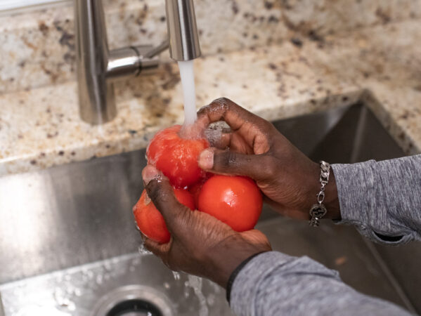 close up of black man's hands washing tomatoes in sink