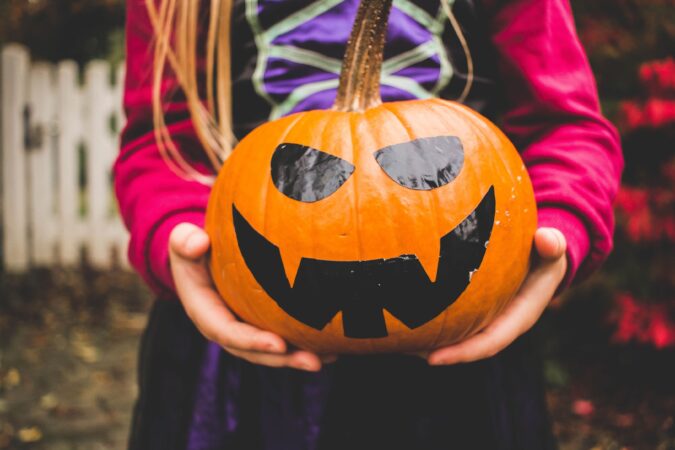 torso of child holding pumpkin with black tape creating a jackolantern face