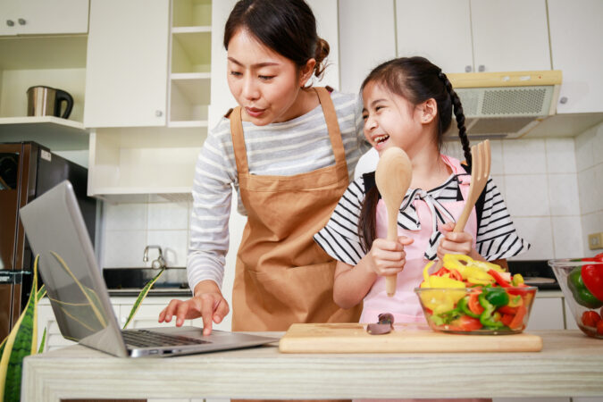 Asian mother and daughter looking at recipe on laptop while preparing salad.
