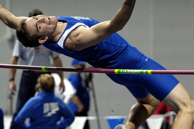 Man in blue track gear arching back over pole.