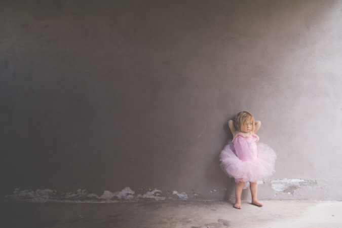 Young child stands in front of blank wall clothed in a pink tutu.
