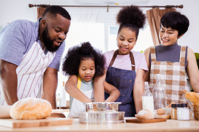 African American family of four cooking in mismatched aprons.