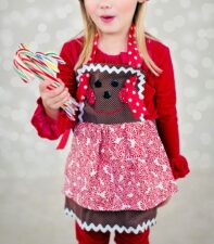 girl in red shirt and gingerbread man two layer apron with rickrak holding candy canes 
