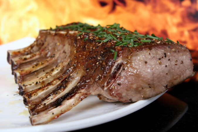 White plate filled with grilled chops and flames in the background.